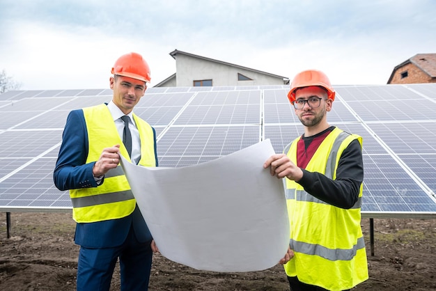 Homens altos em roupas de trabalho estão pensando em instalar painéis solares ao ar livre O conceito de cuidar de painéis solares sob o céu