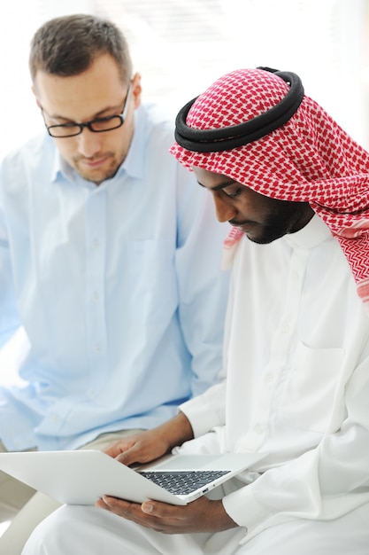 Homens árabes negros e caucasianos trabalhando juntos no laptop