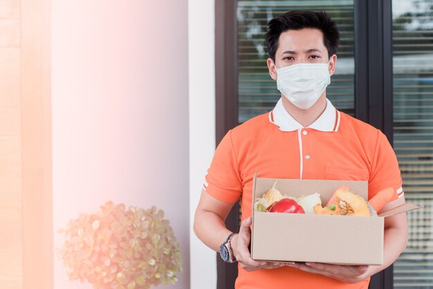 Homens asiáticos carregam mercadorias vestindo uma camiseta laranja manuseie caixas de papel que contêm legumes e frutas