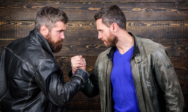 Homens barbudos brutais usam jaquetas de couro apertando as mãos. Aperto de mão forte. Amizade de caras brutais. Símbolo de aperto de mão de um negócio bem sucedido. Acordo comercial aprovado. Significado do gesto de aperto de mão. Concordaram.