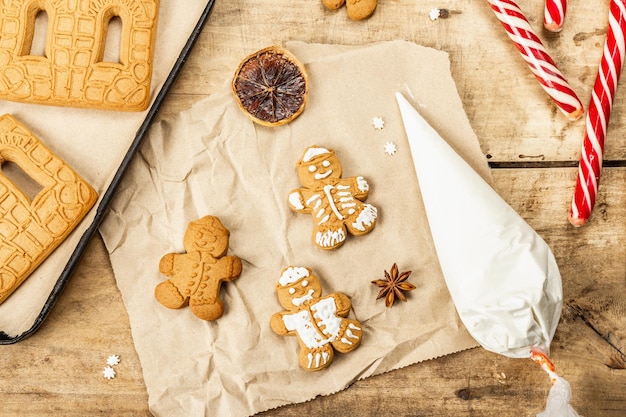 Homens-biscoito decoram glacê doce. Decoração festiva tradicional, processo de cozimento. Fundo de madeira antigo, conceito caseiro, vista superior