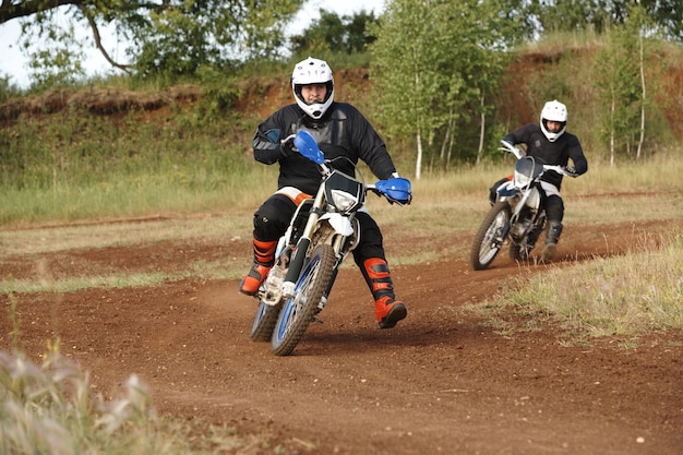 Homens com roupas de proteção, aproveitando o motociclismo em uma estrada suja enquanto competem entre si em uma pista difícil