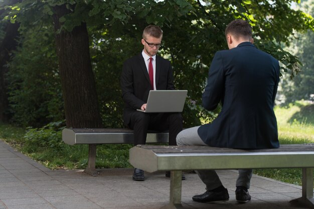 Homens de negócios felizes usando o Tablet Pc fora em um banco de parque