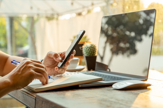 Homens de negócios que usam telefones celulares e escrevendo no caderno com a pena na tabela.