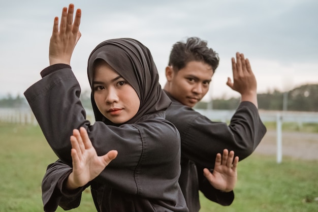 Homens e mulheres asiáticos usando uniformes de silat pencak em pé com movimentos das marés