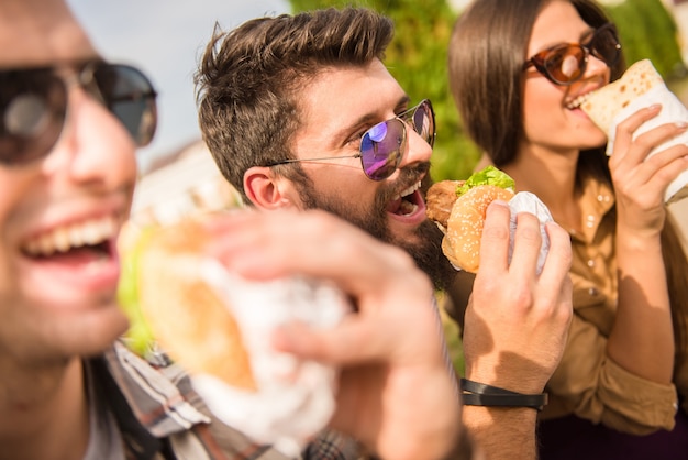 Homens e mulheres estão sentados lá fora e comendo.