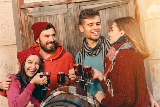 Homens e mulheres europeus sorridentes durante a sessão de fotos da festa. Os caras se passando por amigos no festival de estúdio com uma taça de vinho com vinho quente quente em primeiro plano.