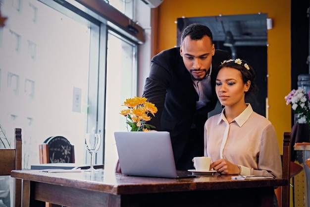 Homens e mulheres negros de negócios afro-americanos bebem café e usam um laptop em um restaurante.