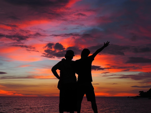 Homens em silhueta de pé contra o céu ao pôr-do-sol