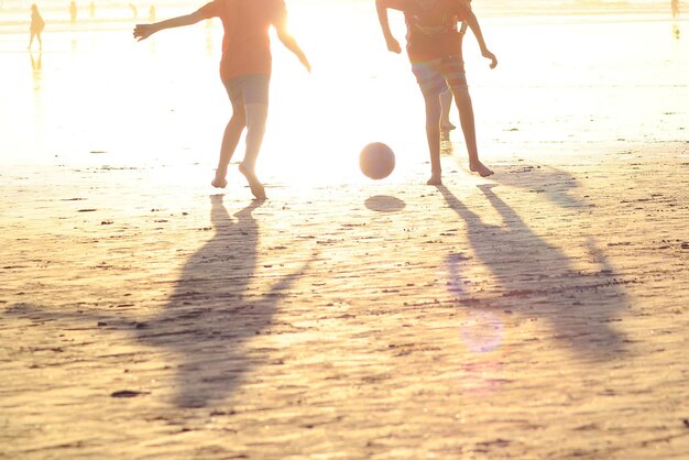 Foto homens em silhueta jogando futebol na praia contra o céu durante o pôr do sol