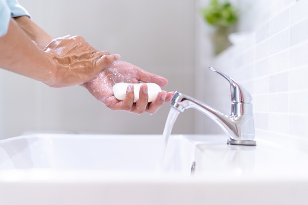 Homens estão lavando as mãos com sabão e água limpa parados na frente da pia dentro do banheiro. A limpeza frequente de mãos e braços evita a propagação de patógenos e vírus.