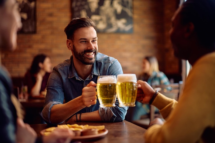 Foto homens felizes a brindar com cerveja num bar.