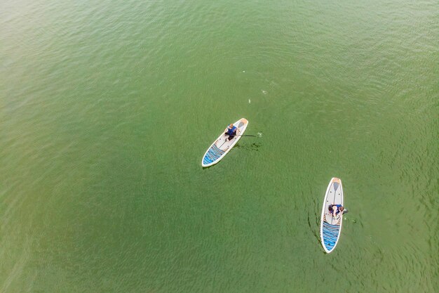 Homens fortes flutuando em pranchas de SUP em uma bela baía em um dia ensolarado Vista aérea dos homens atravessa a baía usando o paddleboard Competições de esportes aquáticos