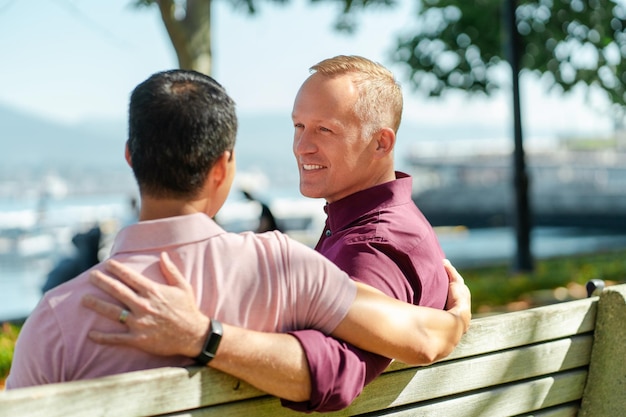 homens gays bonitos homossexuais sentados no banco se abraçando olhando uns para os outros relaxando ao ar livre