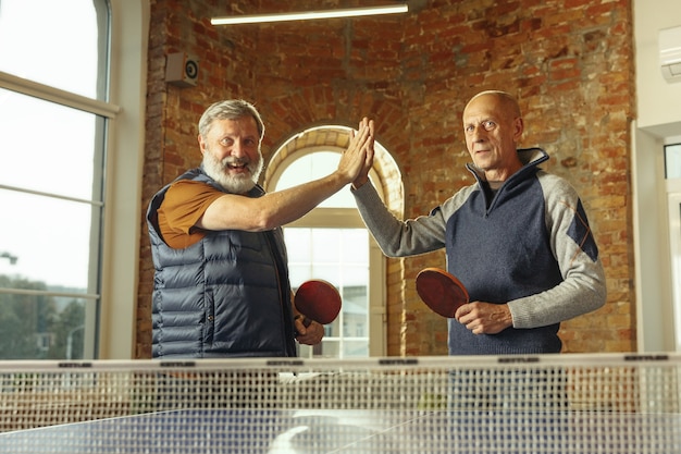 Homens idosos jogando tênis de mesa no local de trabalho se divertindo