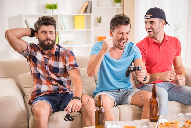 Homens jovens bebem cerveja, comem pizza e jogam jogos play station