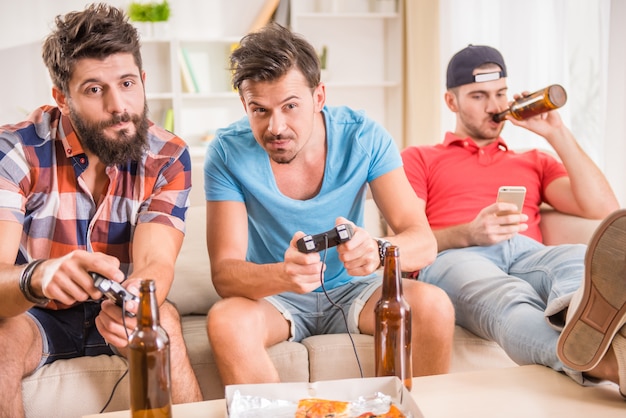 Homens jovens bebem cerveja, comem pizza e jogam jogos play station