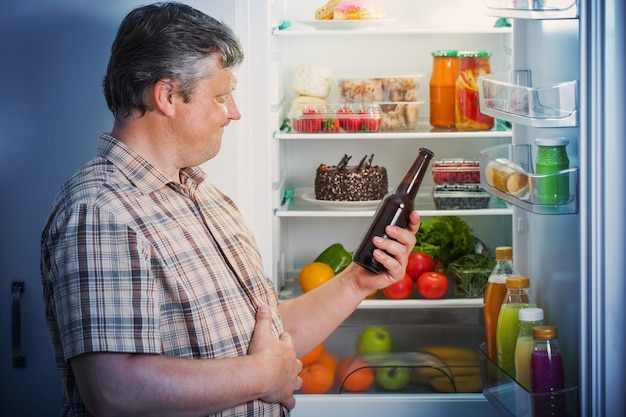 Homens maduros na geladeira com cerveja