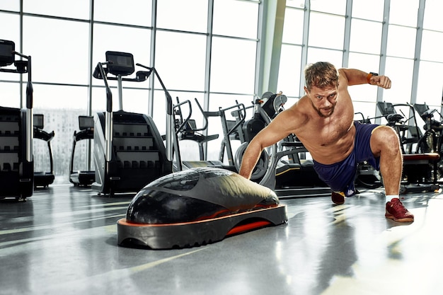 Homens musculosos bonitos se exercitam na plataforma macia de treinamento funcional no ginásio