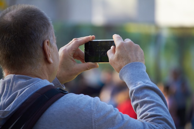 Homens na rua fotografando com telefone celular, plano de fundo é blured cidade
