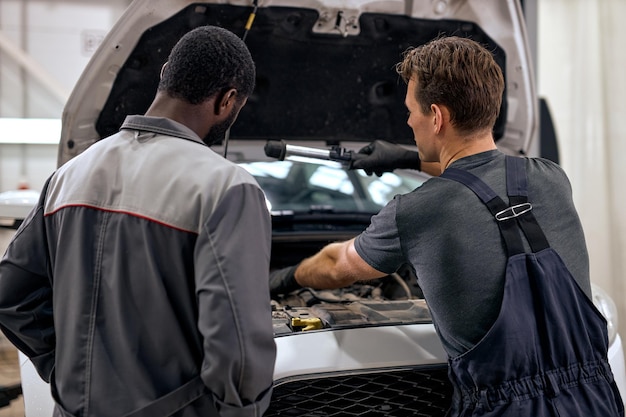 Homens negros e americanos ou caucasianos podem consertar qualquer coisa bonita mecânica de carros em uniforme de macacão chec