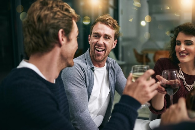 Homens rindo, mulher e copo de vinho brindando em casa ou restaurante de luxo para festa de aniversário de Ano Novo ou evento de celebração Sorria amigos felizes e unidos com bebidas alcoólicas em saudações de sucesso