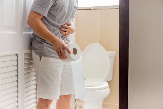 Homens segurando o rolo de papel higiênico têm conceito de sintoma de coronavírus de dor abdominal.