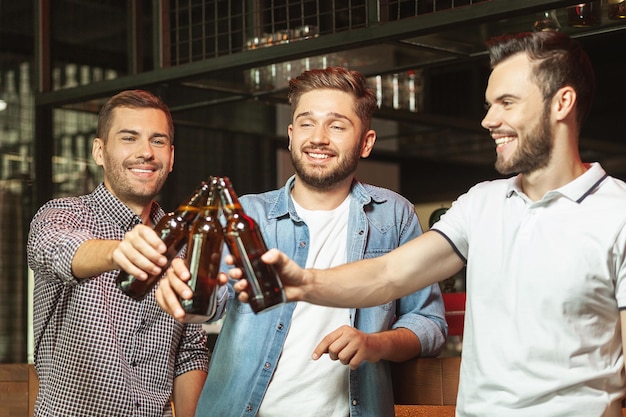 Foto homens sorridentes clicando com garrafas de cerveja no bar