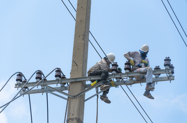 Homens técnicos consertando ou consertando linha de força quebrada em poste elétrico, trabalho altamente perigoso.