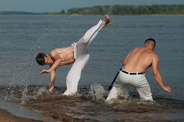 Homens treinam capoeira na praia