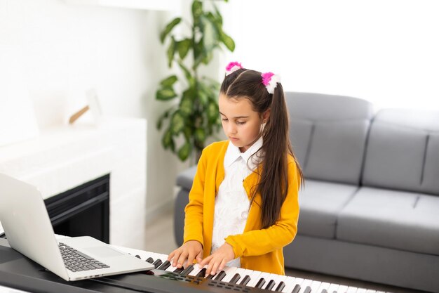 Homeschool garotinha aprendendo piano do computador conectando-se à aula on-line de música na internet pelo professor da escola. Novo estilo de vida normal e educação, estudo estudantil em casa conceito.