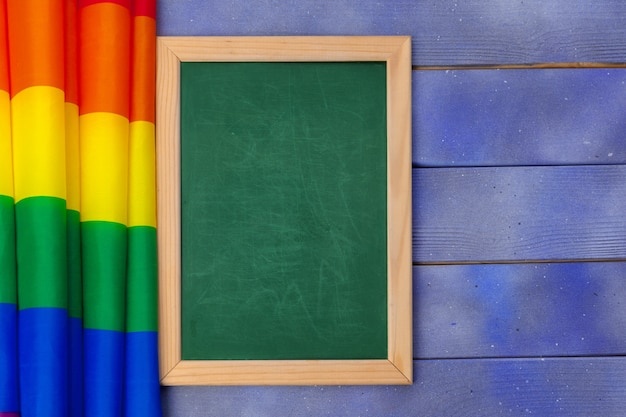 Homosexuelle Flagge des hellen Regenbogens auf hölzernem Hintergrund und leerem Greenboard