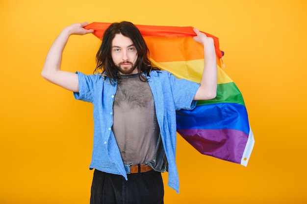 Homosexueller Mann mit einer Gay-Pride-Flagge, die auf gelbem Hintergrund lächelt und wegschaut