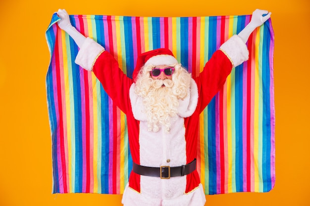 Homosexueller weihnachtsmann, der die lgbt-flagge hält. weihnachten gay pride-konzept. gay santa claus auf gelbem hintergrund. der weihnachtsmann ist schwul