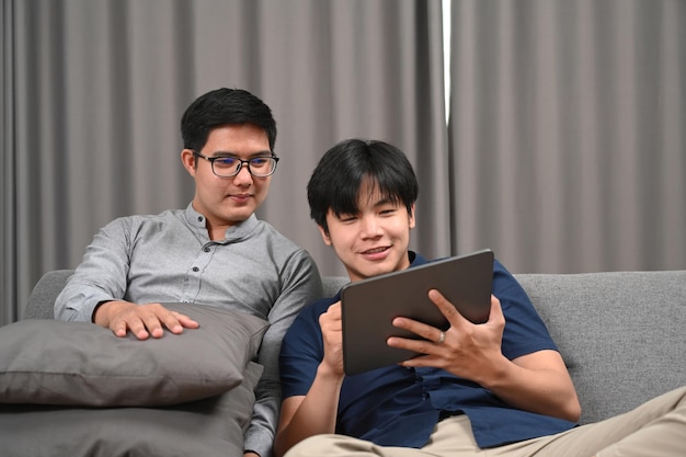 Homosexuelles Paar, das digital zusammen auf einem bequemen Sofa verwendet