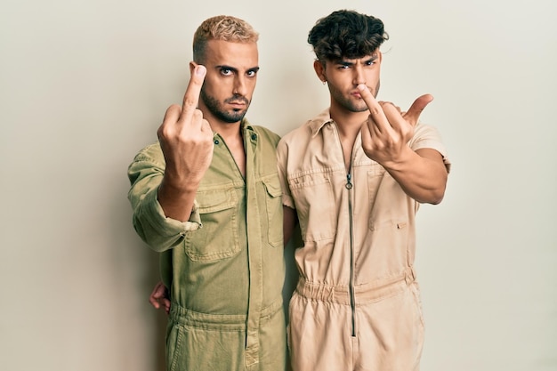 Homosexuelles schwules Paar, das zusammensteht und einen legeren Overall trägt, der den Mittelfinger zeigt, unhöflichen und unhöflichen Gesichtsausdruck