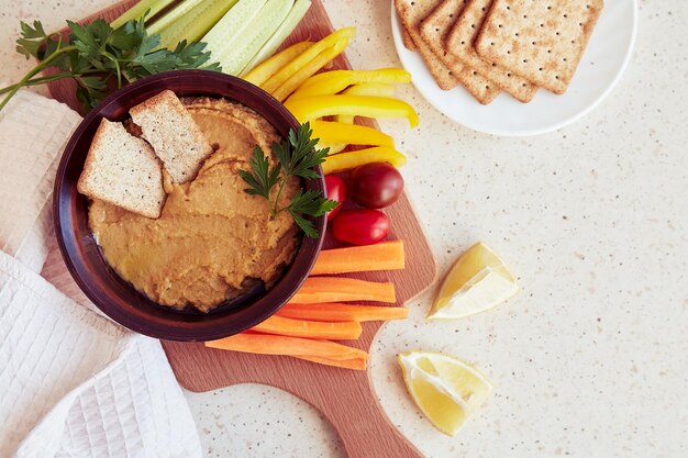 Homus caseiro com biscoitos de grãos salsa limão e legumes frescos em uma tábua de corte Lanches vegetarianos saudáveis Copiar espaço