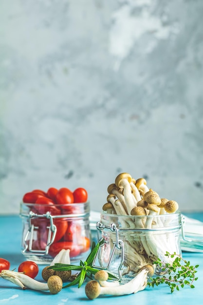 Hongo comestible Buna Shimeji del este de Asia Buena comida para una buena salud Grupo de hongos shimeji y tomates cherry en frascos sobre fondo de superficie de hormigón azul