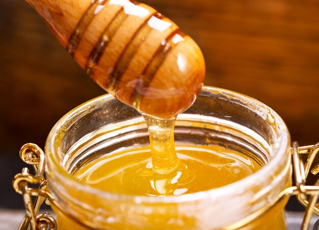 Honig, der vom Schöpflöffel in ein Glas auf einem Holz gießt