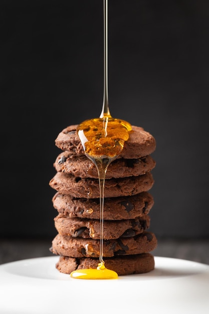 Honig gießt auf hausgemachte Schokoladenkekse auf dunklem Hintergrund in Nahaufnahme. Komposition aus selbstgemachten Keksen, über die Schokoladenstücke und Honig gegossen werden. Dessert