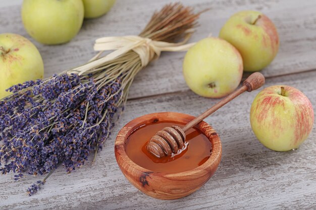 Honig in Holzschale mit Honiglöffel, grünen Äpfeln und Lavendelblüten auf weißem Vintage-Holzhintergrund