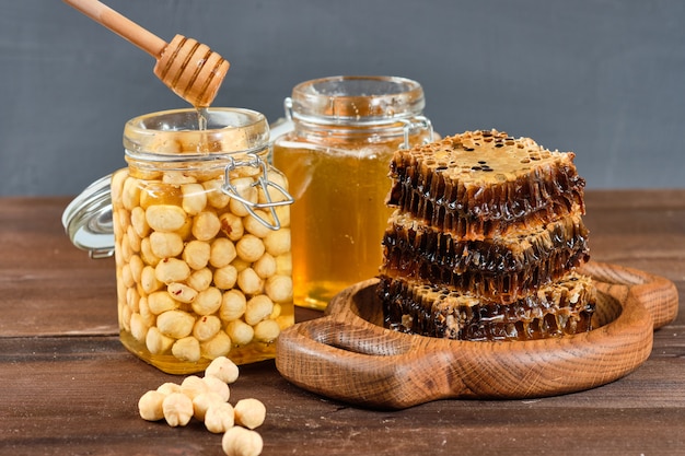 Honig in Waben auf einem Holzteller und goldener Honig in Gläsern mit Nüssen