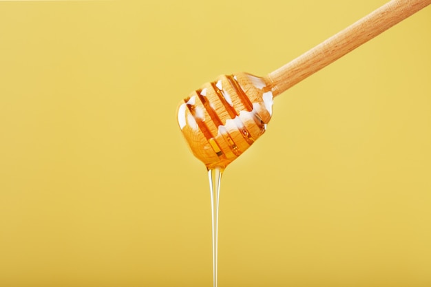 Honig tropft in einem dünnen Strahl aus einem Honiglöffel auf gelbem Grund