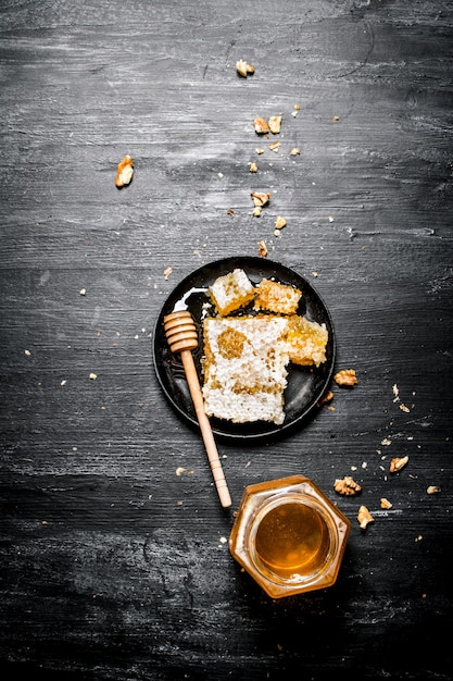 Honigart Ein Glas natürlicher Honig und Honigkamm in der Pfanne auf schwarzem rustikalem Hintergrund