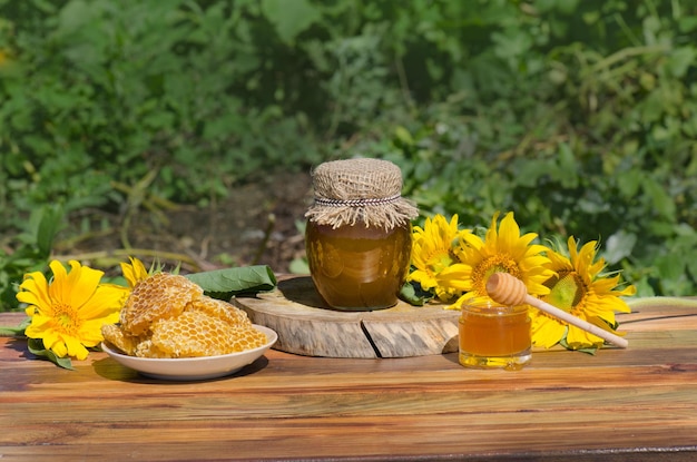 Honigglas und Holzstab auf dem Tisch vor grün verschwommenem natürlichen Hintergrund Honigglas und Waben auf Holztisch im Freien