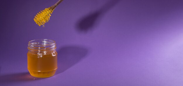 Honiglöffel schwebt über einem Glas süßen Bio-Naturhonigs auf tiefem lila Hintergrund
