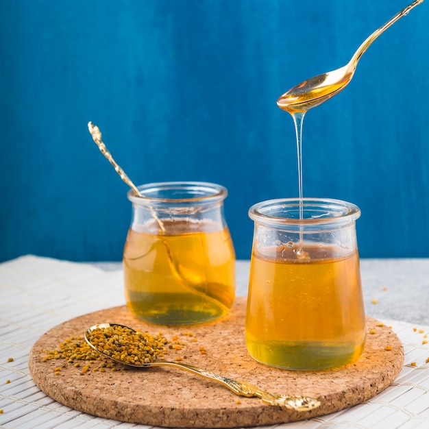 Honigtöpfe und Löffel mit Bienenpollen auf Korkenuntersetzer