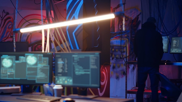 Hooded Hacker kommen in einem versteckten neon beleuchteten unterirdischen Schutzraum mit Graffiti an