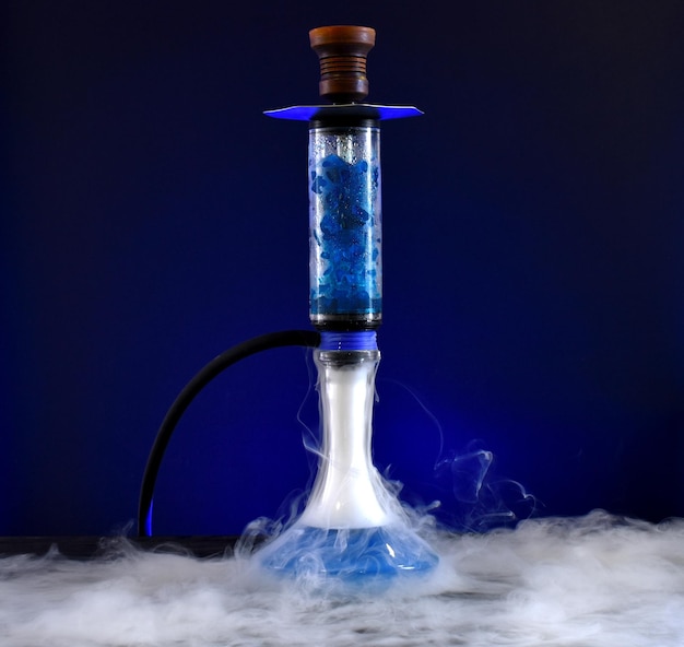 Hookah con matraz de vidrio y cuenco de barro con humo sobre fondo oscuro