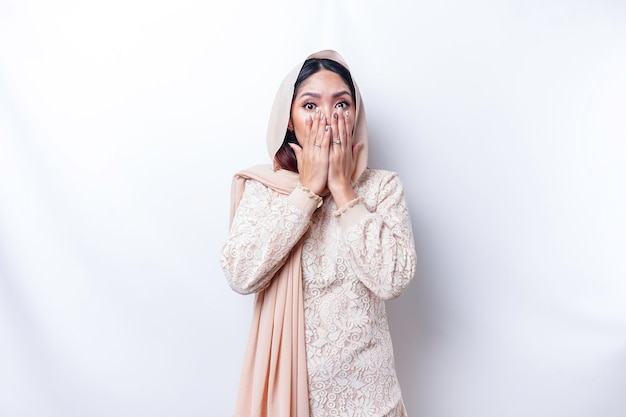 Hoppla Überrascht junge asiatische Muslimin, die den Mund mit den Händen bedeckt und in die Kamera starrt, während sie vor weißem Hintergrund steht